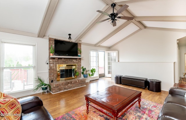living area featuring ceiling fan, a fireplace, a wainscoted wall, wood finished floors, and vaulted ceiling with beams