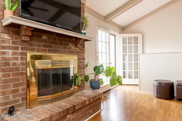 interior space with a wainscoted wall, vaulted ceiling with beams, wood finished floors, and a fireplace