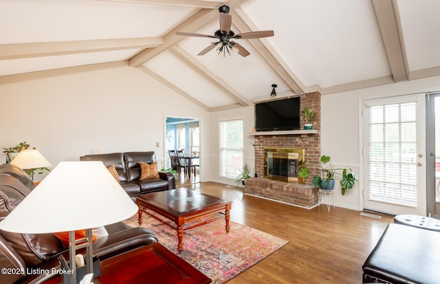 living area featuring a brick fireplace, a ceiling fan, lofted ceiling with beams, and wood finished floors
