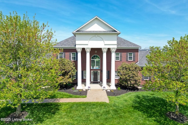 neoclassical home featuring roof with shingles and a front yard