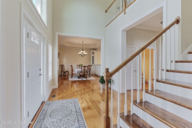 entrance foyer featuring stairway, crown molding, light wood finished floors, and a towering ceiling