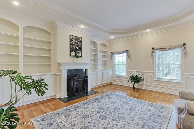 living room with a premium fireplace, visible vents, built in features, and light wood finished floors