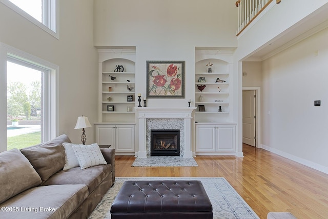 living area with a fireplace, a high ceiling, baseboards, and light wood-type flooring