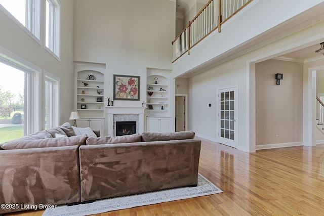 living room with ornamental molding, a towering ceiling, wood finished floors, baseboards, and a lit fireplace
