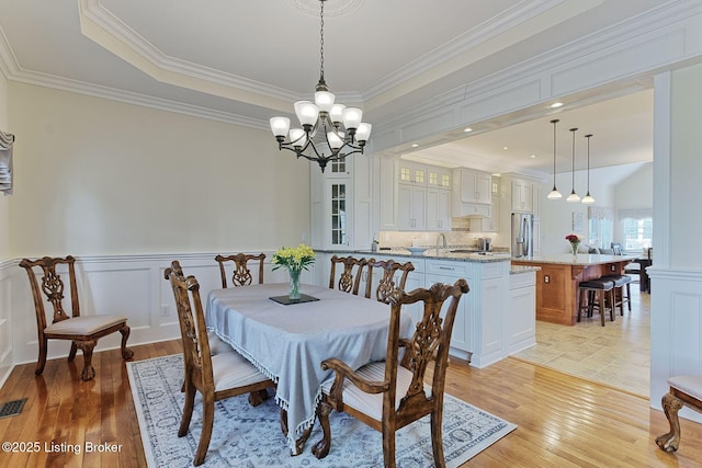 dining area featuring crown molding, an inviting chandelier, wainscoting, and light wood-style flooring