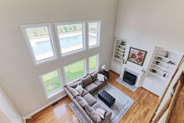 living area with a fireplace with flush hearth, built in shelves, a high ceiling, and light wood-style flooring