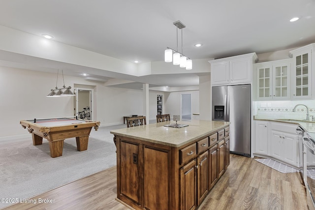 kitchen with light stone countertops, glass insert cabinets, light wood-style floors, stainless steel fridge with ice dispenser, and a sink