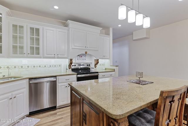 kitchen featuring a breakfast bar area, appliances with stainless steel finishes, light stone countertops, a sink, and white cabinetry