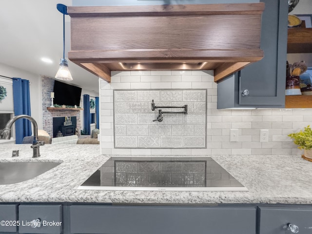 kitchen featuring tasteful backsplash, a brick fireplace, black electric cooktop, a sink, and premium range hood