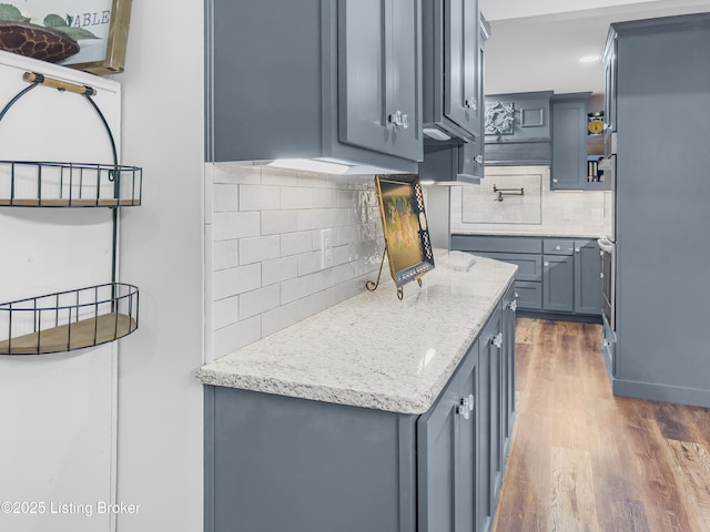 kitchen with light stone counters, decorative backsplash, wood finished floors, and double oven