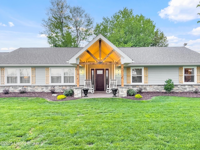 view of front of property with a front lawn, roof with shingles, and stone siding