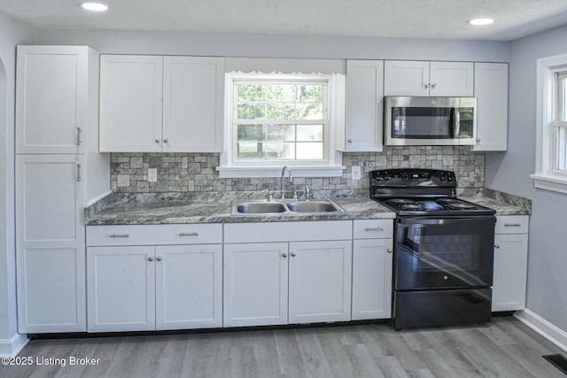 kitchen with stainless steel microwave, white cabinets, a sink, light wood finished floors, and black / electric stove