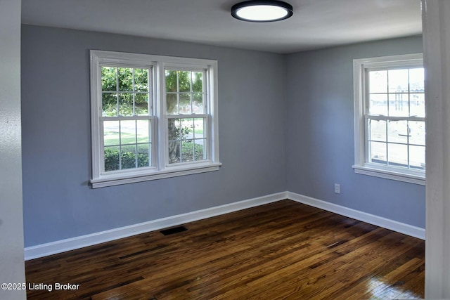 unfurnished room with baseboards, dark wood-style flooring, a healthy amount of sunlight, and visible vents