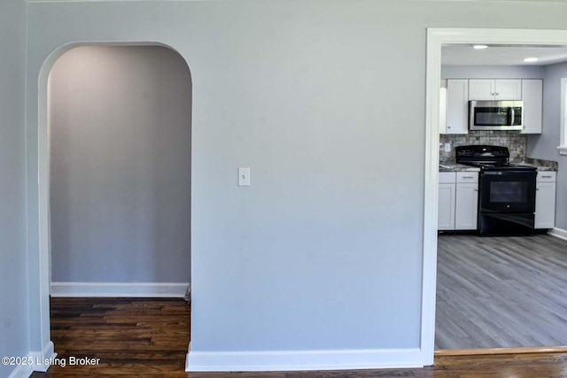 kitchen with dark wood-type flooring, white cabinetry, stainless steel microwave, black range with electric stovetop, and arched walkways