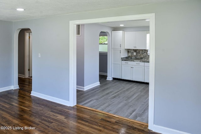 kitchen featuring white cabinets, arched walkways, baseboards, and dark wood-type flooring