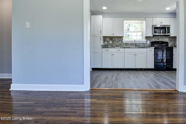 kitchen featuring a sink, baseboards, stainless steel microwave, wood finished floors, and black range with electric cooktop