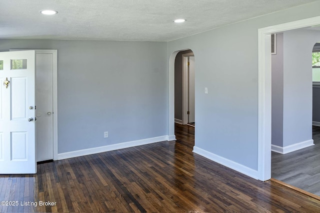 unfurnished room featuring arched walkways, baseboards, and dark wood finished floors