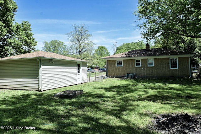 rear view of property with a chimney, central AC unit, brick siding, fence, and a yard