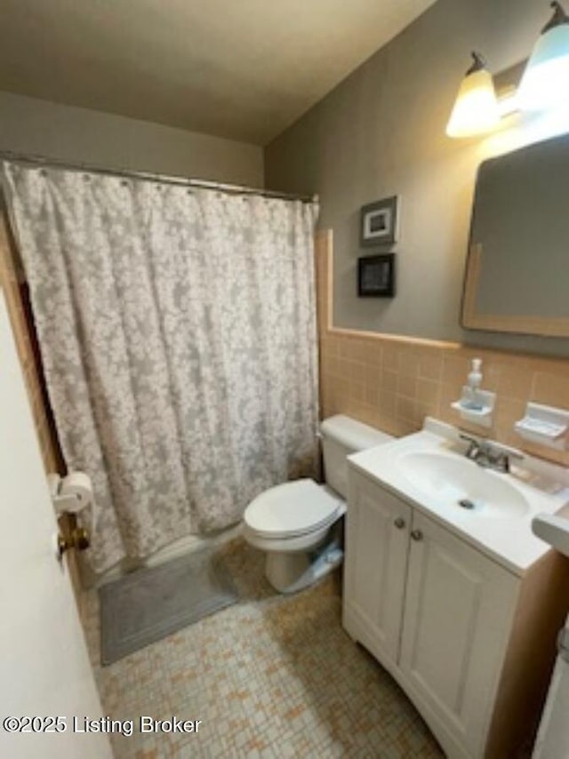 full bathroom featuring tile walls, wainscoting, curtained shower, vanity, and toilet