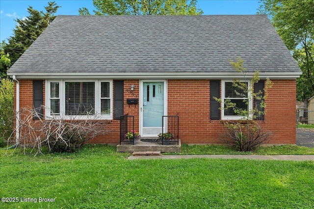 view of front of house featuring roof with shingles, a front lawn, and brick siding