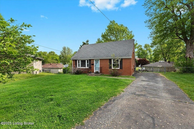 view of front facade featuring fence, driveway, brick siding, and a front yard