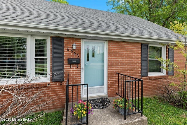 doorway to property featuring brick siding and a shingled roof