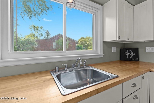 kitchen with a sink, wood counters, and white cabinets