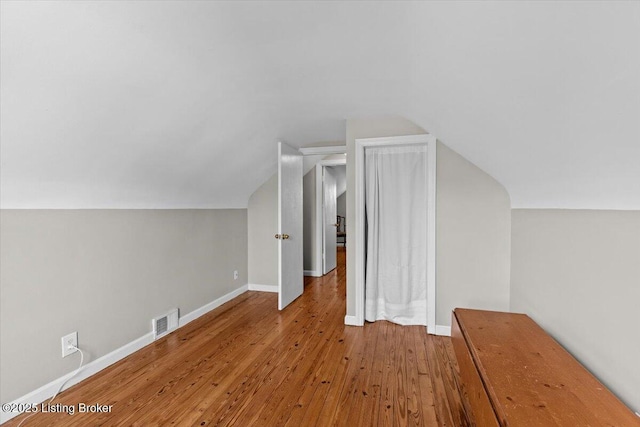 additional living space featuring baseboards, wood-type flooring, vaulted ceiling, and visible vents