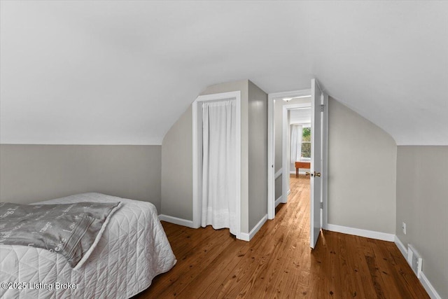 bedroom featuring baseboards, visible vents, wood finished floors, and lofted ceiling