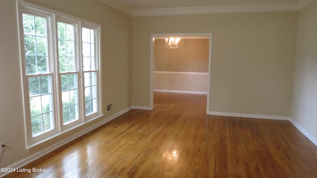 unfurnished room featuring an inviting chandelier, crown molding, wood finished floors, and a wealth of natural light