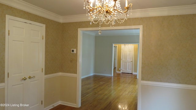 empty room with crown molding, baseboards, a chandelier, and wood finished floors