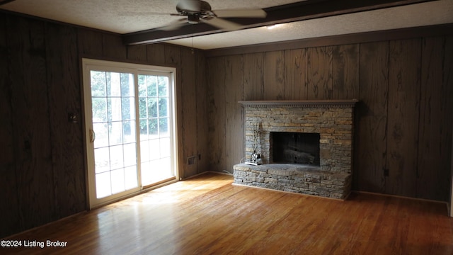 unfurnished living room with wood walls, wood finished floors, beam ceiling, ceiling fan, and a textured ceiling