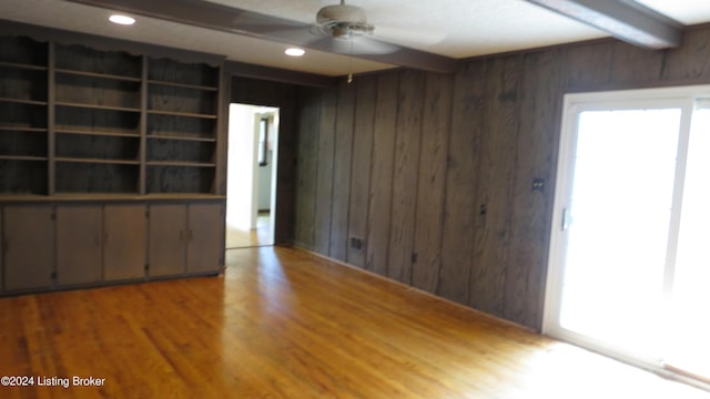 interior space with wooden walls, a ceiling fan, beam ceiling, and wood finished floors
