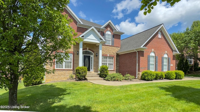 traditional home with roof with shingles, a front yard, brick siding, and stone siding