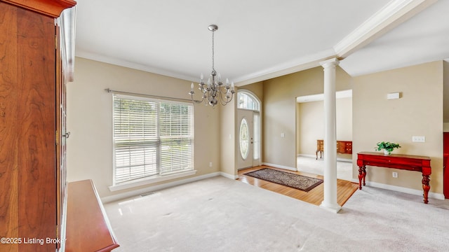 carpeted entrance foyer featuring baseboards, decorative columns, ornamental molding, and an inviting chandelier