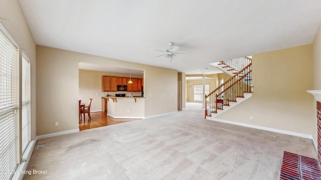 unfurnished living room featuring stairway, baseboards, ceiling fan, and light colored carpet