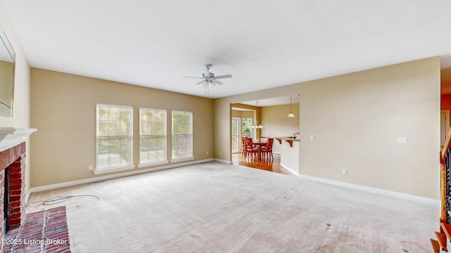 unfurnished living room with baseboards, ceiling fan, a fireplace, and carpet flooring