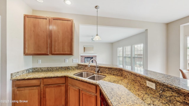 kitchen featuring brown cabinets, light stone counters, a sink, recessed lighting, and decorative light fixtures