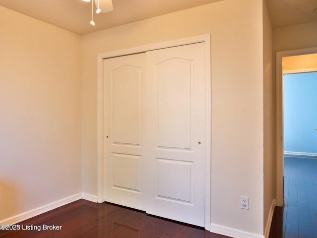 unfurnished bedroom with baseboards, a closet, and dark wood-style floors