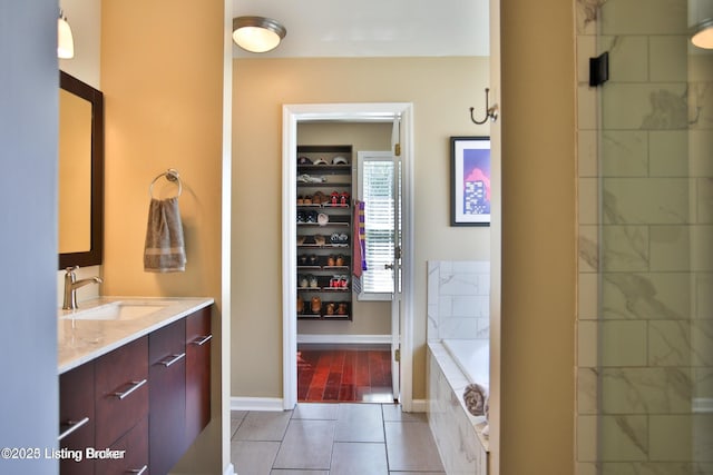 bathroom with tile patterned flooring, baseboards, tiled tub, and vanity