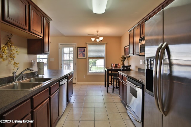 kitchen featuring dark countertops, a sink, a notable chandelier, stainless steel appliances, and light tile patterned flooring