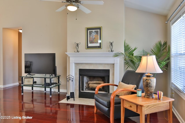 living area featuring a tiled fireplace, baseboards, ceiling fan, and wood finished floors