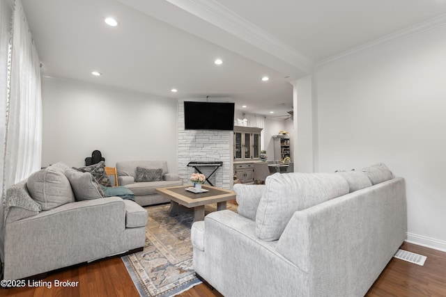 living area featuring crown molding, recessed lighting, a stone fireplace, and wood finished floors