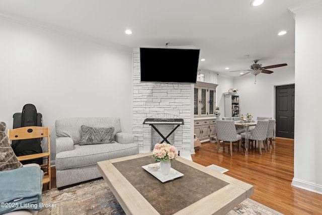 living area with ornamental molding, a stone fireplace, ceiling fan, recessed lighting, and light wood-style flooring