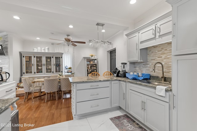kitchen with decorative backsplash, ceiling fan, a sink, a peninsula, and ornamental molding