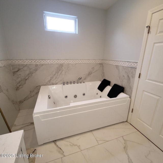 bathroom featuring a tub with jets, marble finish floor, wainscoting, and tile walls