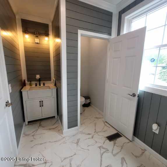 bathroom featuring wooden walls, toilet, marble finish floor, and vanity