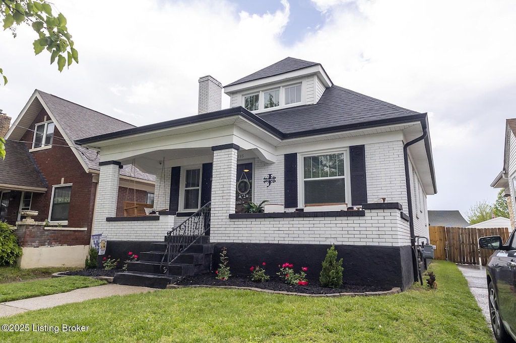 bungalow-style home with covered porch, brick siding, a chimney, and a front lawn