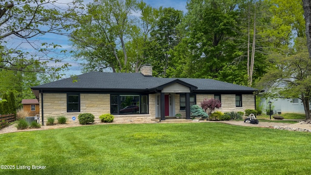 view of front of house featuring a chimney, roof with shingles, a front yard, fence, and stone siding
