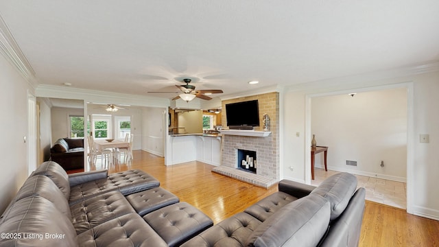 living area with a ceiling fan, a fireplace, light wood-type flooring, baseboards, and ornamental molding